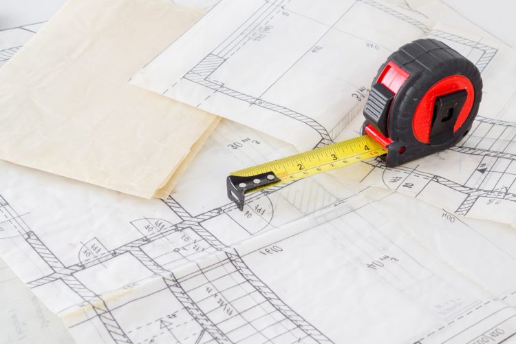 A measuring tape is laid across the top of different architectural drawings