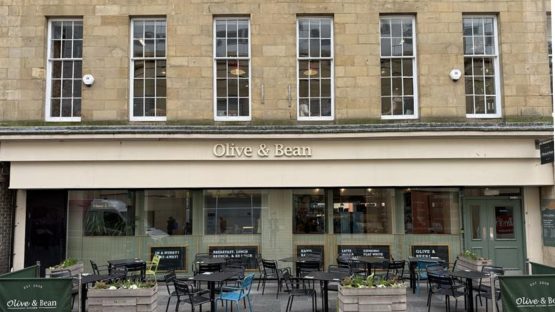 A photo of the Olive and Bean frontage in the Grainger Market Newcastle. Stone building with seating out the front